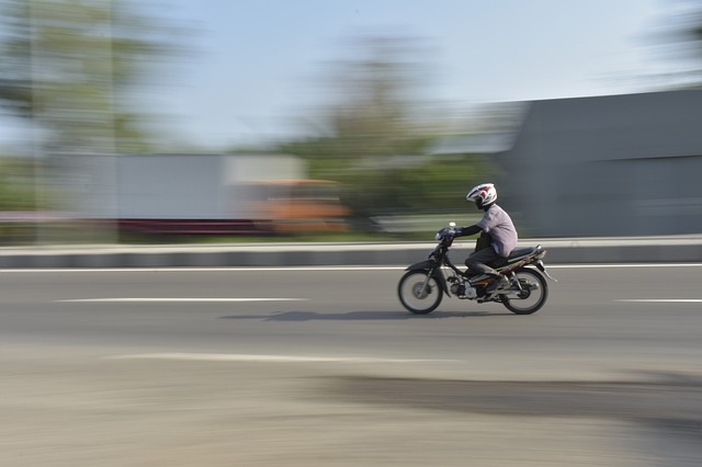 Muž s prilbou na hlave ide po ceste na motorke